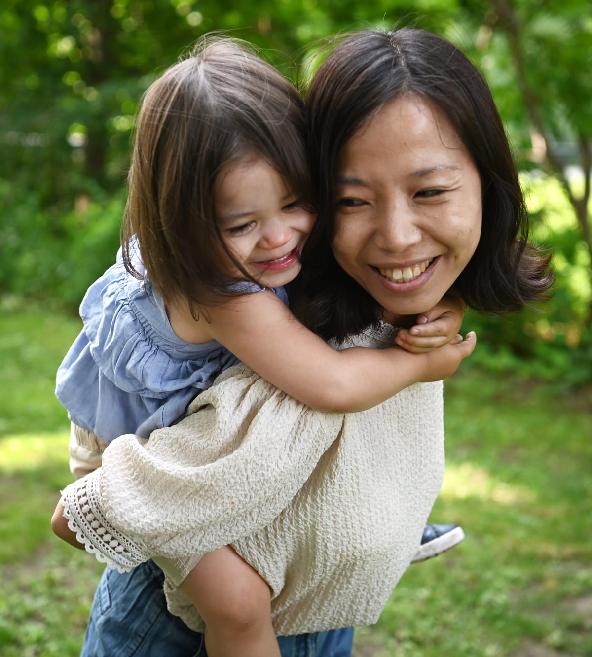 Gem giving a child a piggyback in a sunlit park